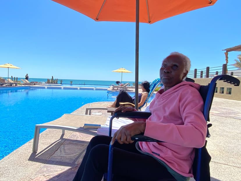 Mami in a pink hoodie by a resort pool, orange parasol behind her