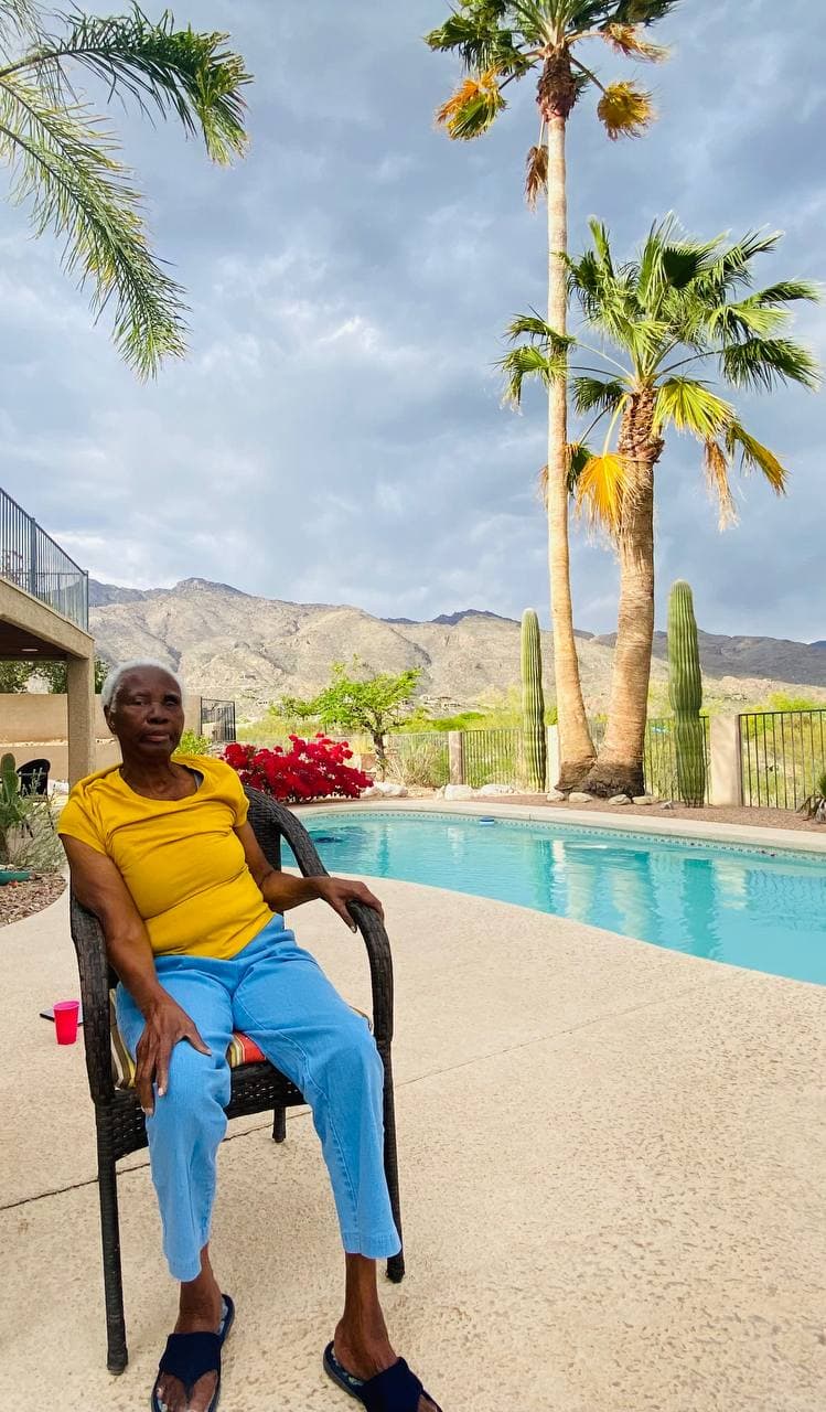 Mami in a yellow t-shirt, full-length outdoor portrait with palms and mountains